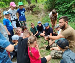 Grupa dzieci wraz z instruktorami podczas zajęć z survivalu, na świeżym powietrzu.