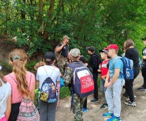 Grupa dzieci wraz z instruktorami podczas zajęć z survivalu, na świeżym powietrzu.