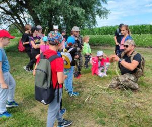 Grupa dzieci wraz z instruktorami podczas zajęć z survivalu, na świeżym powietrzu.