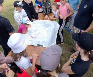 Grupa dzieci wraz z instruktorami podczas zajęć z survivalu, na świeżym powietrzu.