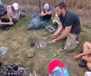 Grupa dzieci wraz z instruktorami podczas zajęć z survivalu, na świeżym powietrzu.