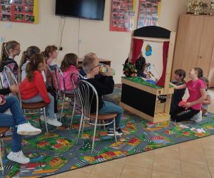 Zdjęcie przestawia grupę dzieci bawiące się w teatr wewnątrz budynku.