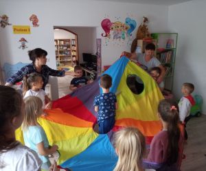 Na zdjęciu widoczna jest grupa dzieci wewnątrz budynku bawiąca się chustą animacyjna