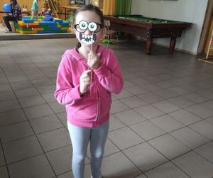 Na zdjęciu widoczna jest dziewczynka wewnątrz budynku, trzymająca przy twarzy przebranie z foto budki.