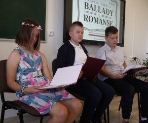 Uczniowie klasy szóstej - dwóch chłopców i dziewczynka z wiankiem z kwiatów na głowie, czytający balladę