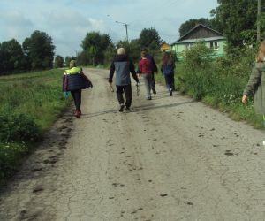 Grupa uczniów pod opieką dyrektora zbiera  śmieci przy drodze w kierunku świetlicy. 