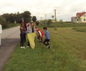 Grupa uczniów sprząta pobocza drogi.