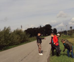 Uczniowie wraz z nauczycielką  porządkują  pobocza w kierunku kapliczki. 