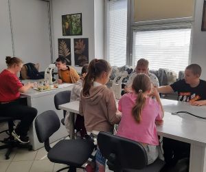 Uczniowie siedzą przy stolikach, grupa pierwsza rozpoznaje kwiaty roślin łąkowych ,a druga grupa poznaje i degustuje produkty pszczelarskie.