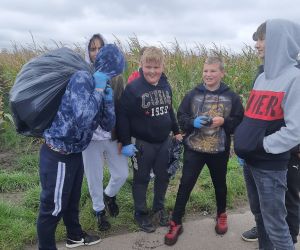 Chłopiec niesie na plecach worek pełen śmieci i przechodzi obok kolegów z klasy