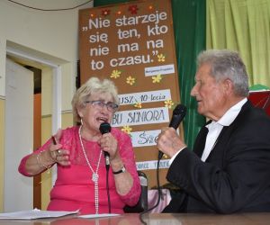 Mężczyzna w garniturze trzyma teczkę w dłoniach.W tle grupa osób w odświętnych ubraniach.