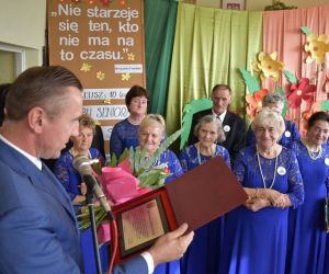 Kobieta i mężczyzna siedzą przy stole, oboje trzymają mikrofony.