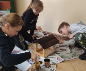 Na zdjęciu widoczna jest grupa dzieci malująca karmnik dla ptaków.