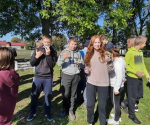 Uczniowie stoją przy ognisku i jedzą pieczone ziemniaki
