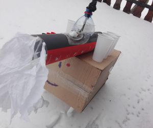 Konstrukcja z kartonowych pudeł, i plastikowych elementów, stoi na śniegu.