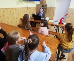 Dzieci razem z osobą prowadzącą zajęcia, w klasie.