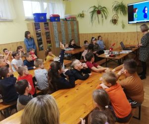 Dzieci razem z osobą prowadzącą zajęcia, w klasie.