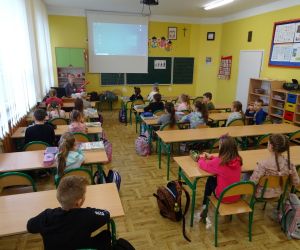 Dzieci razem z osobą prowadzącą zajęcia, w klasie.