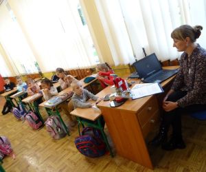 Dzieci razem z osobą prowadzącą zajęcia, w klasie.