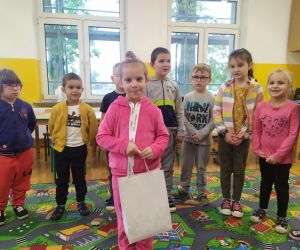 Solenizantka Ola stoi w środku koła z torbą, w której są cukierki, dookoła stoją dzieci.