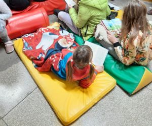 Dziewczynka leży na materacu okryta kocykiem i czyta książkę
