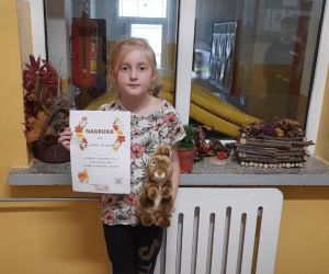 Uczennica trzyma w ręku dyplom i nagrodę otrzymaną za udział w konkursie o jesieni