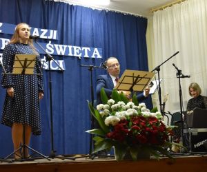 Osoba występuje na scenie. Osoby prowadzące koncert znajdują się z boku.