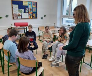 Pracownik biblioteki rozmawia z uczniami, którzy siedzą w kręgu na krzesełkach