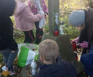 Uczniowie z nauczycielką zapalają znicze na mogile