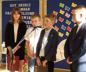 Uczennica i trzech uczniów klasy siódmej w strojach galowych przy mikrofonie