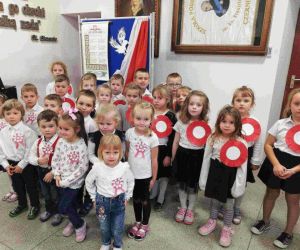 Przedszkolaki w strojach galowych i z kotylionami narodowymi śpiewają hymn państwowy