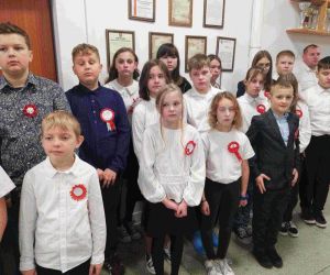 Uczniowie klasy piątej i szóstej w strojach galowych i z kotylionami narodowymi śpiewają hymn państwowy