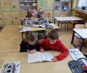 Dzieci siedzą w ławkach i oglądają książeczki