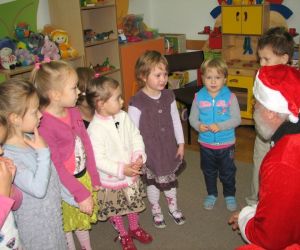 Dzieci z Mikołajem, stoją w klasie lekcyjnej. W tle widać materiały edukacyjne oraz zabawki.