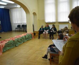 Zdjęcie przedstawia zgromadzonych wewnątrz budynku gości. Na scenie widoczna jest dziewczynka.