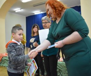 Zdjęcie przedstawia kobietę i dziecko. Kobieta gratuluje dziecku poprzez uściśnięcie dłoni i wręczeniu nagrody.