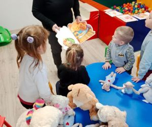 Na zdjęciu widoczne są dzieci słuchające jak pani czyta im książeczkę.