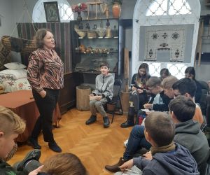 Prowadząca warsztaty opowiada o tradycjach andrzejkowych, uczniowie siedzą i słuchają