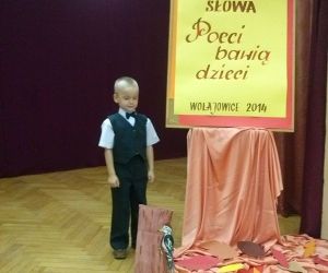 Chłopiec, pozuje do zdjęcia na scenie. Tablica z napisem: Turniej Sztuki i Słowa, Poeci bawią dzieci.