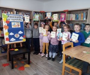 Na zdjęciu widoczne są dzieci pozujące do zdjęcia na tle regałów z książkami.