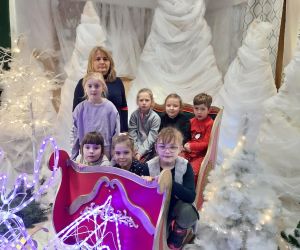 Uczniowie z nauczycielką siedzą w  czerwonych saniach Mikołaja