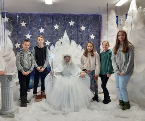 Uczniowie stoją, a w środku siedzi na tronie Królowa Śniegu