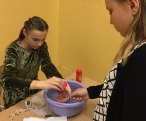 Uczennica wróży z wosku, przed nią stoi inna dziewczynka