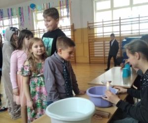 Uczennica wróży z wosku, przed nią stoi kilku uczniów z klas młodszych