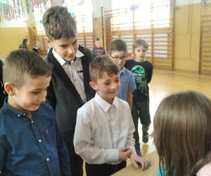 Kilku uczniów stoi przed stolikiem, na którym znajdują się kubeczki z wróżbą