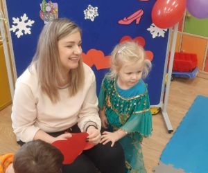 Dziewczynka stoi obok nauczycielki trzymającej w dłoniach czerwone papierowe serce