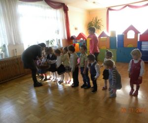 Dzieci stoją w rzędzie, nauczycielka częstuje je owocami