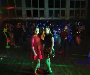 Dziewczynki w odświętnych sukienkach tańczą na sali gimnastycznej