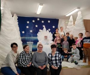 Zdjęcie przedstawia grupę osób dorosłych i dzieci pozujących do zdjęcia w scenerii zimowej.