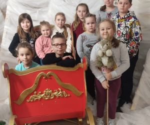 Zdjęcie przedstawia grupę dzieci pozujących do zdjęcia w otoczeniu zimowej scenerii.